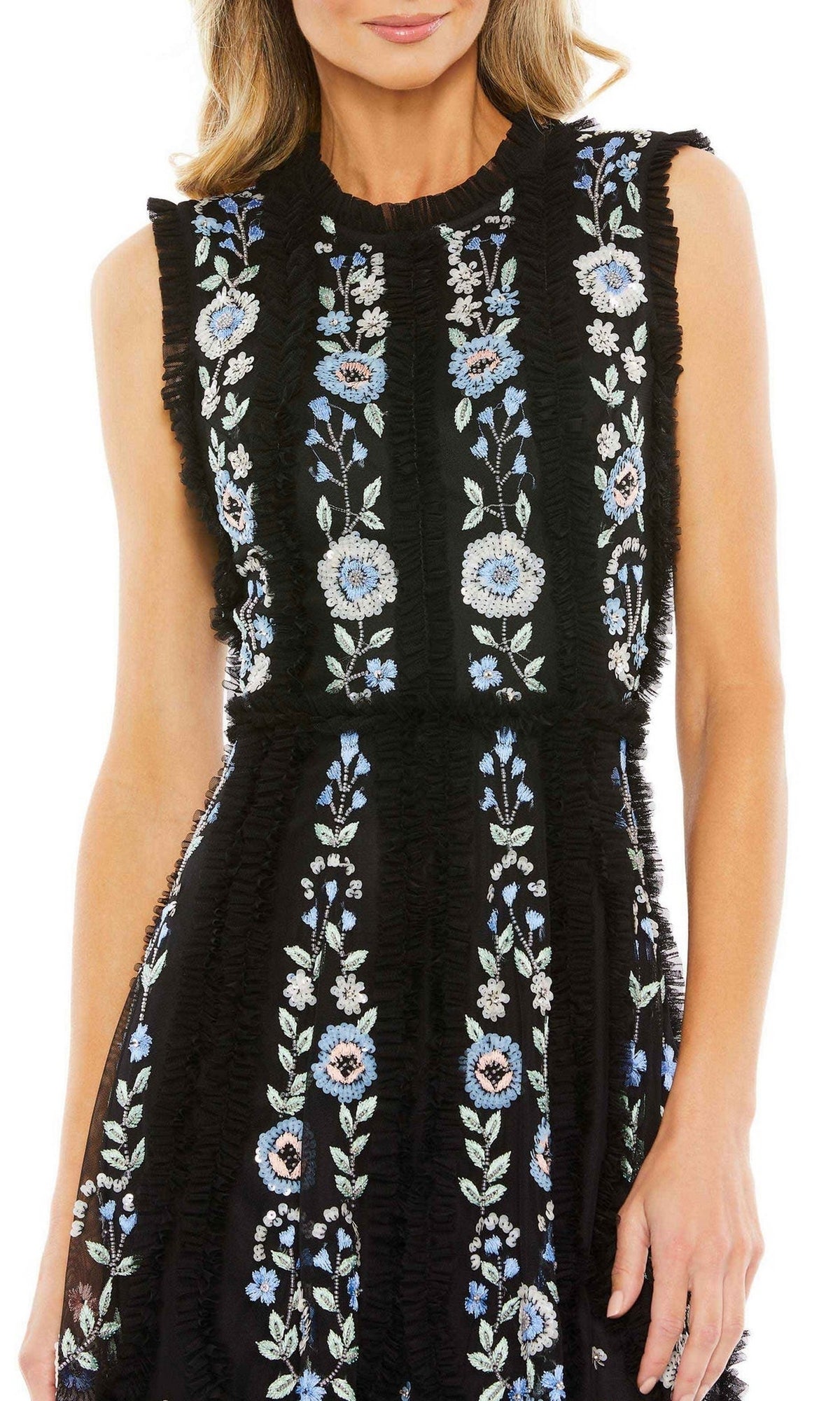 A woman wears the Mac Duggal 9135 Embroidered Short Party Dress—sleeveless, black, with light blue, white, and green floral embroidery—standing against a white background.